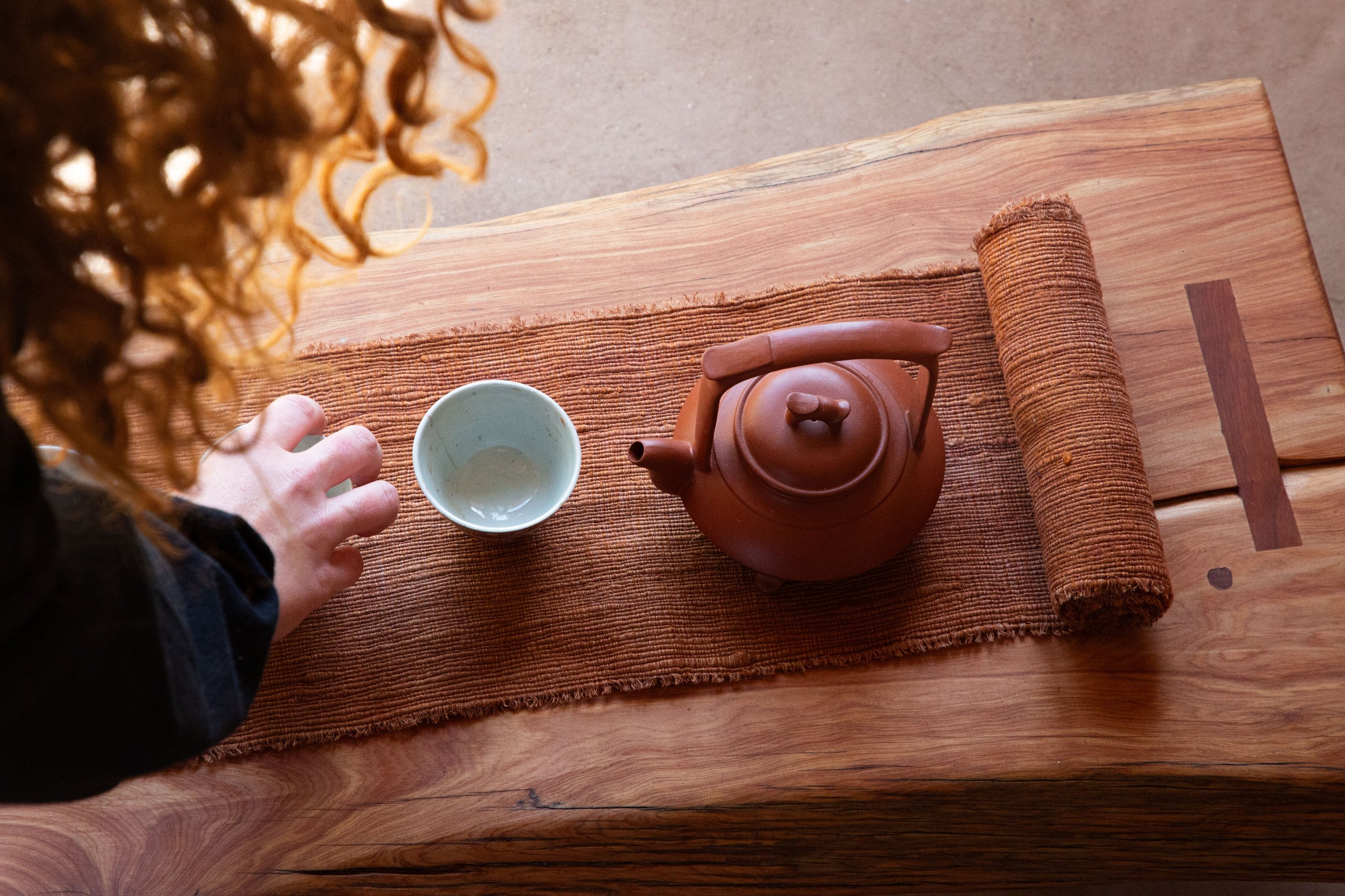 Tea set on a wooden table with a person's hand reaching for a teacup.