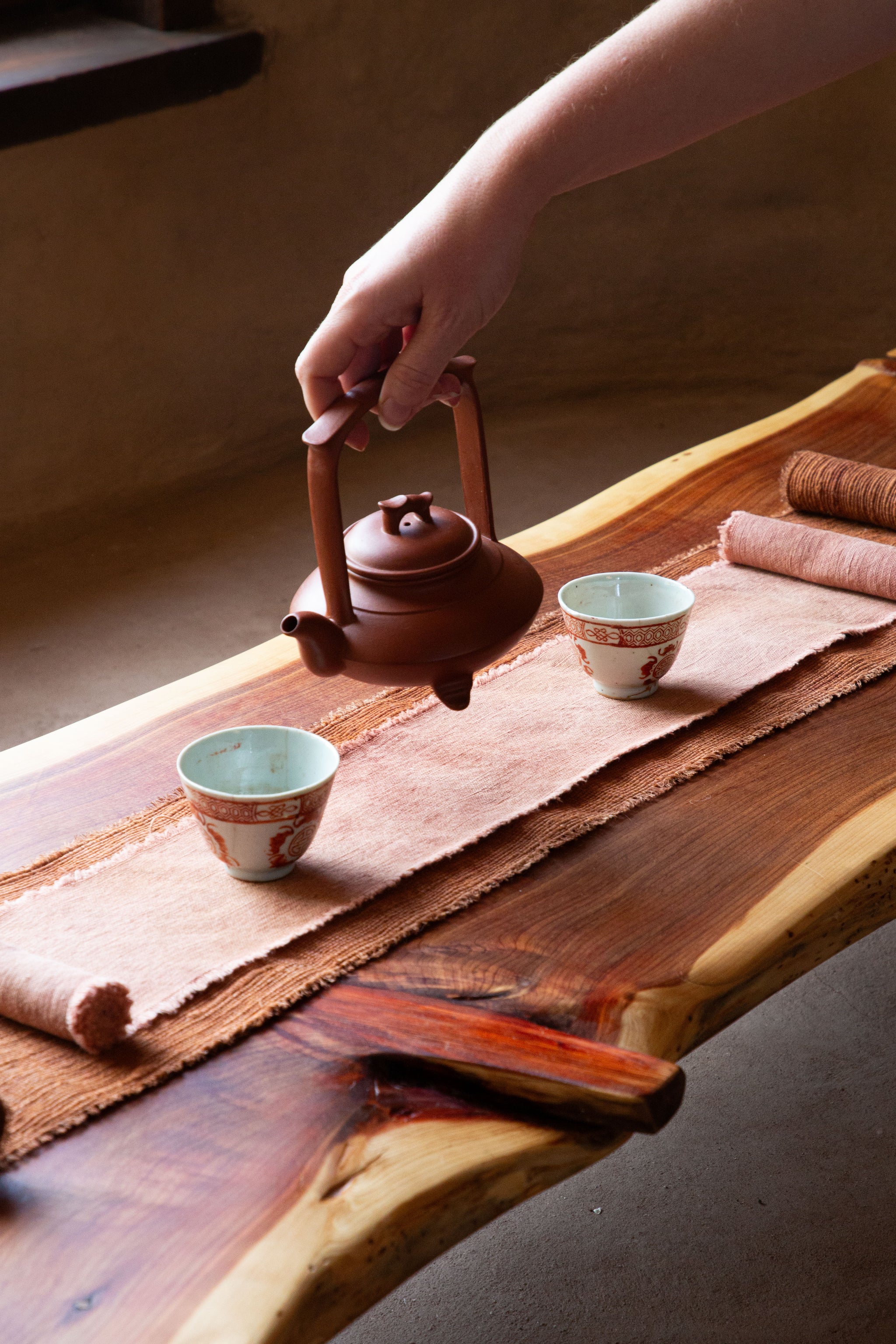 Person pouring tea from a traditional teapot into two cups on a wooden table.